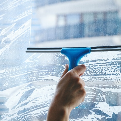 young female hand cleaning dirty glass window with a squeegee